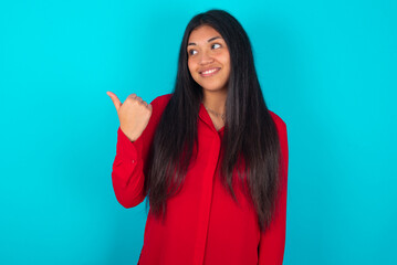 young latin woman wearing red shirt over blue background points away and gives advice demonstrates advertisement