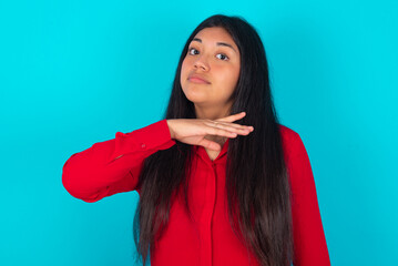 young latin woman wearing red shirt over blue background cutting throat with hand as knife,...