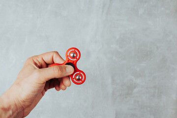 Man hand holding red plastic fidget spinner on marble background. Anti stress toy