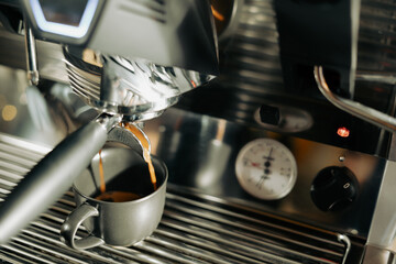 Close-up image of the coffee machine in a coffee shop or restaurant. Barista making coffee extraction from a professional modern espresso brewing machine by a bottomless filter. Cafe Service Concept