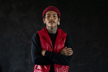 Portrait of cool Asian hip hop young bearded man with tattoo on face, neck and hands standing and...