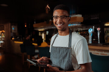 African American male waiter smiling holding digital tablet
