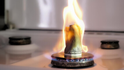 Concept of gas crisis. One hundred dollar bill is burning on a kitchen stove burner. Cash money....