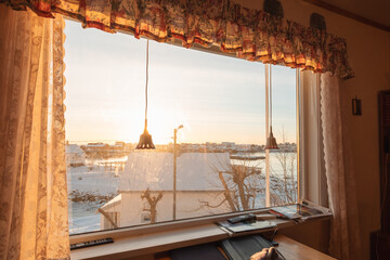 View from curtain window with sunset over snowy village on coastline in winter