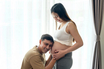 Young pregnant woman with husband embracing and expecting a baby at home