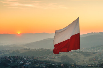 Biało-czerwona flaga Polski na tle zachodzącego słońca w górach - Ochodzita, Koniaków