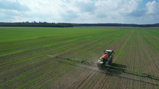 Modern agricultural machinery. Self-propelled sprayer with high ground clearance and long booms works in the field. Feeding crops at the germination stage. View from a drone flying around a sprayer.