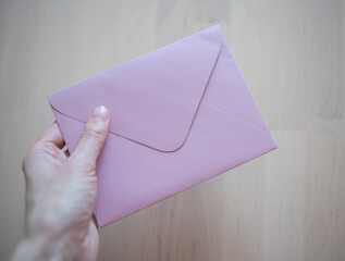 an envelope of pink color, made of paper, on a wooden surface of the table. Message, transmission...