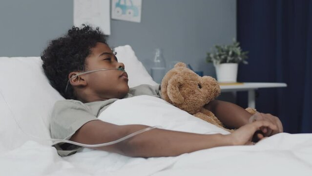 Medium of adorable African American boy sleeping with stuffed bear in hospital bed, then waking up and smiling