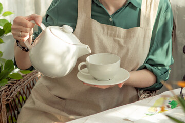 a girl pours tea from a white teapot into a white cup on the veranda