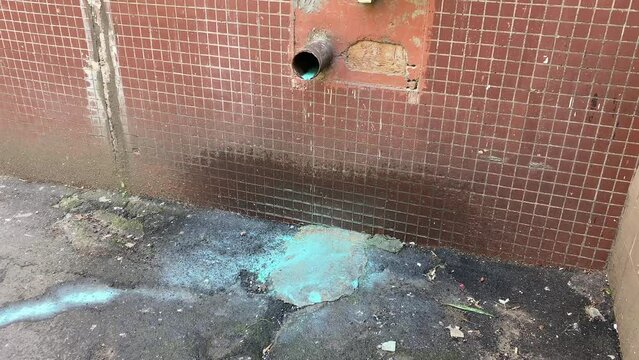 Dirty blue water runs out of a rusty pipe in a wall