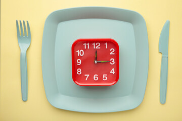 Top view of red alarm clock with plate, fork and knife on yellow background - concept and idea