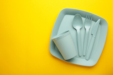 Bright plastic reusable tableware on a yellow background.