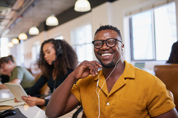 A Black man smiles at the camera wearing glasses in the office
