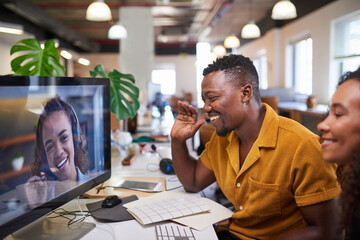 A Black man waves to his colleague on a video call from his office - obrazy, fototapety, plakaty