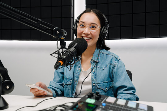 Young female radio host using microphone and headphones in studio