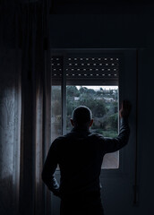 Rear view of adult man looking through window in bedroom