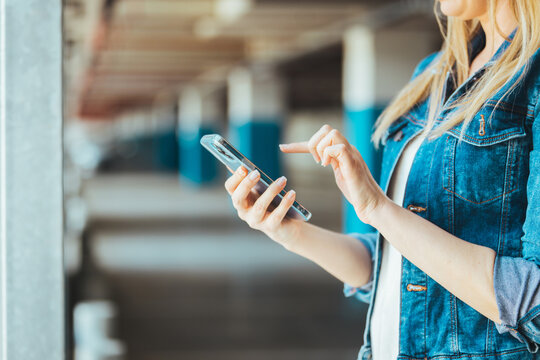 Photo of Young business woman wearing casual clothing calling mobile phone while standing with blurred car in parking lot. Side view of Beautiful, happy Caucasian female using smartphone device