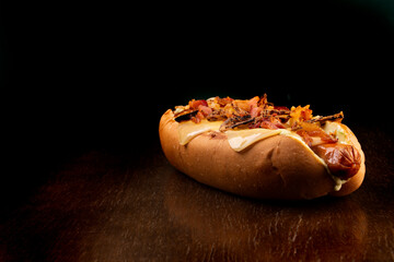 typical gourmet american hot dog with bacon, melted cheese and crispy onion on wooden table close up