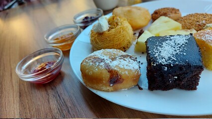Dessert auf einem weißen Porzellanteller. Orientalische Kekse. Schokoladenwürfel mit Kokos. Kadaif-Kuhen mit Walnüssen. Donuts. Sesamkuchen. Gläser mit Fruchtmarmelade. Orangensaft und Kaffee. Kaffee