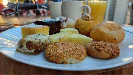 Dessert auf einem weißen Porzellanteller. Orientalische Kekse. Schokoladenwürfel mit Kokos. Kadaif-Kuhen mit Walnüssen. Donuts. Sesamkuchen. Gläser mit Fruchtmarmelade. Orangensaft und Kaffee. Kaffee