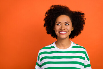 Portrait of attractive bewildered cheerful girl deciding copy blank space isolated over bright orange color background