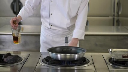 A chef in a white uniform creating a flambe with alcohol. Cooking pan catching fire. Flames in a kitchen. Slow motion footage.