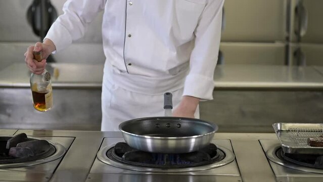 A chef in a white uniform creating a flambe with alcohol. Cooking pan catching fire. Flames in a kitchen. Slow motion footage.