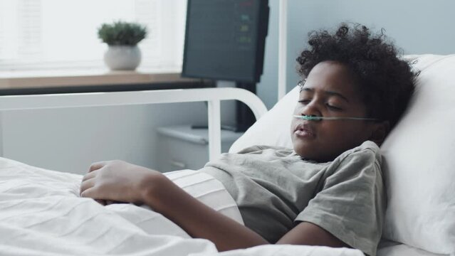 Medium of African American boy with oxygen tube in nose sleeping in hospital bed at daytime