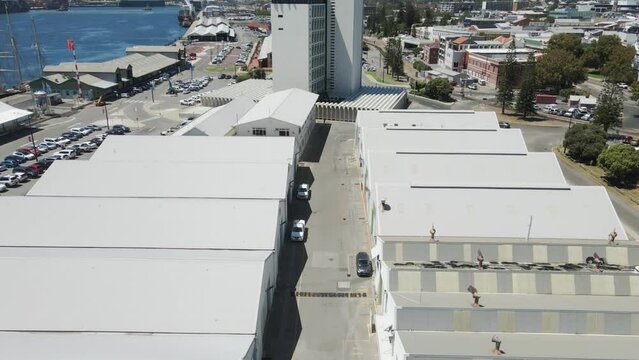 An onward moving aerial shot above white warehouses built beside each other in a row. The primary function of a warehouse is to provide storage space for equipment, inventory or other items.
