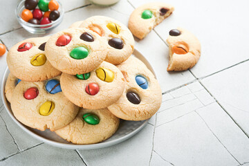Homemade cookies with colorful chocolate candies and milk. Stack of shortbread cookies with multi colored candy on plate with bottle of milk on light gray background. Baby food concept. Copy space.