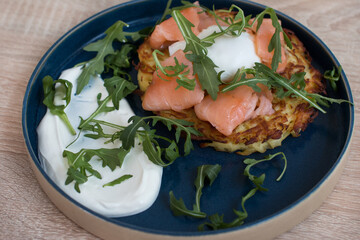 Fried draniki with red salted fish and poached egg. A dish decorated with herbs and sour cream