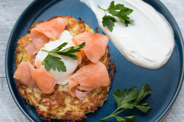 Fried draniki with red salted fish and poached egg. A dish decorated with herbs and sour cream