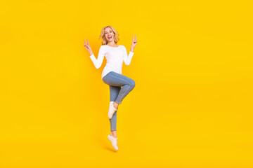 Fototapeta na wymiar Full body photo of funny young blond lady jump v-sign wear shirt jeans shoes isolated on yellow background
