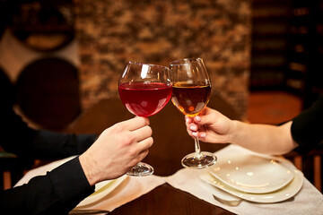 Cheers with wine glasses. Close up. Young couple in love on a date in a restaurant. The boy and the girl are resting in a cozy place and drinking wine