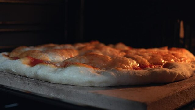 Cheese melting process on pizza from oven heat. Delicious pizza richly strewn with cheese is cooked in the oven. Tasty Italian pizza cheese roasted in the oven on a stone. High quality 4k video