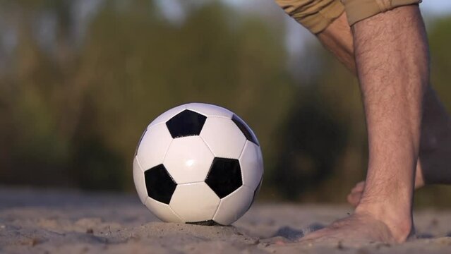 Close-up of Kicking Soccer Ball. Slow Motion. Man's Foot Kicks Ball Lying on Sand