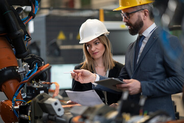 Chief engineer and project manager in modern industrial factory with robot arms talking and...