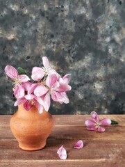 Branch of beautiful pink chinese apple tree flower in the clay pot on the wooden table against black concrete background with copy space. Still life with spring flowers.