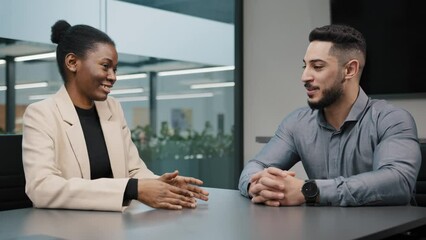 Arabic businessman and African businesswoman talking at office table. Two partners female manager and male boss negotiating in company. Colleagues woman and man workers discussing corporate project