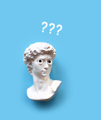 Plaster sculpture head of David with google eyes and question marks image on blue background....