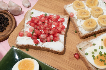 Bread has cream cheese and pomegranate boiled egg banana on pink background.