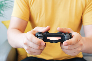 Man in a yellow t-shirt sits on sofa and holds a video game joystick.