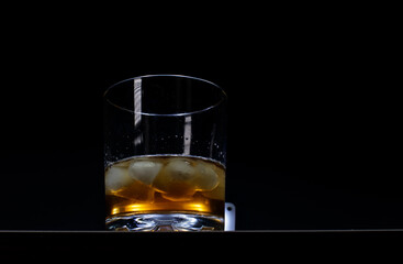 Elegant glass of whiskey with ice cubes on black background with reflection