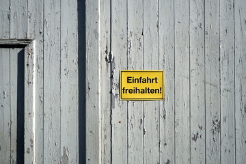 Altes Scheunentor aus Holz in Pastellfarben eines alten Bauernhof mit gelbem Schild Einfahrt...