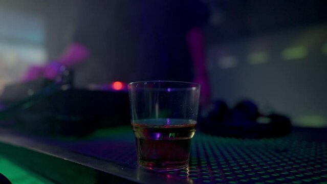 DJ works at console with glass of alcohol on foreground