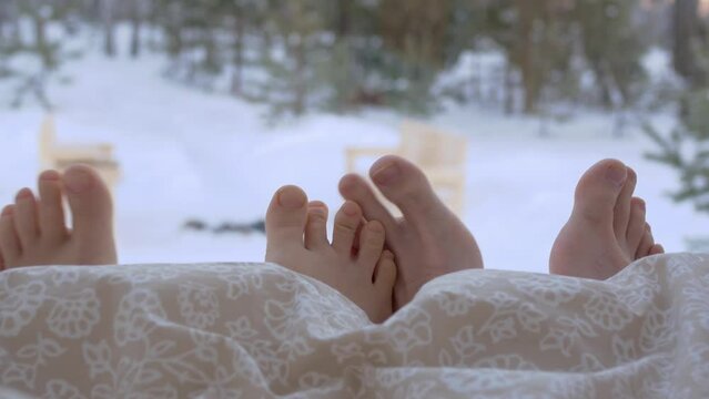 Close-up of toes under a blanket, male and female legs in the bed of a country house overlooking the winter landscape. Man and woman in bed in the morning under a warm blanket.