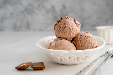 Three brown chocolate ice cream balls, scoops in white bowl on gray background