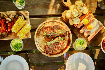 Top view Served with plates dinner table, summer picnic outdoor at home backyard on fresh air, appetizers variety serving on party with grilled vegetables, lemonade, steak, camembert cheese.