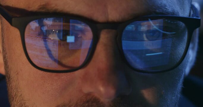 Concentrated man follows data with eyes extreme close view. Reflection of computer screen image on programmer glasses in office. Writing programs